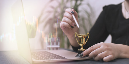 Triumph in Real Estate Investment: A Trophy Representing Success, Model House, and a Laptopの写真素材