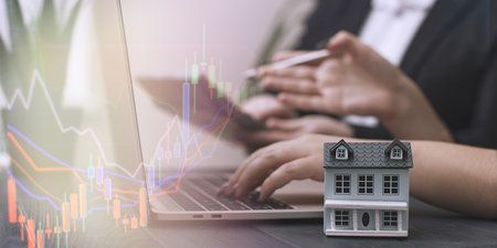 Triumph in Real Estate Investment: A Trophy Representing Success, Model House, and a Laptopの写真素材