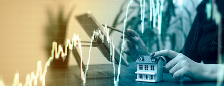 Professionals Reviewing Data with Miniature House Model and Stock Market Candlestick Chart Overlay in a Businessの写真素材