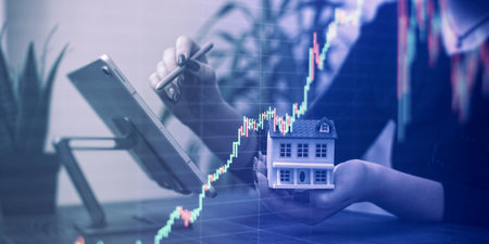Professionals Reviewing Data with Miniature House Model and Stock Market Candlestick Chart Overlay in a Businessの写真素材