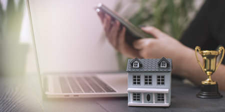Triumph in Real Estate Investment: A Trophy Representing Success, Model House, and a Laptopの写真素材