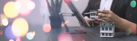 Professionals Reviewing Data with Miniature House Model and Stock Market Candlestick Chart Overlay in a Businessの写真素材