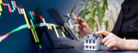 Professionals Reviewing Data with Miniature House Model and Stock Market Candlestick Chart Overlay in a Businessの写真素材