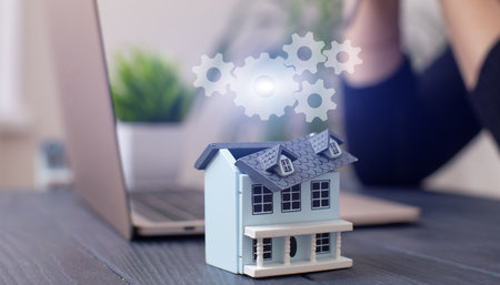 Businesswoman Facing Challenges in Real Estate Investment: Model House on a Desk with Laptop in a Modern Workspace Settingの写真素材