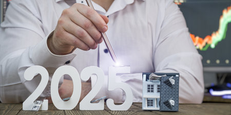 2025 Real Estate and Financial Growth Concept: Hand with Stylus Lighting Up Numbers and Model House with Stock Market Chart in theの写真素材