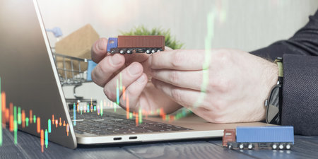 businessman holding a miniature truck over a laptop with stock market graphs, symbolizing logistics, supply chain investmentの写真素材