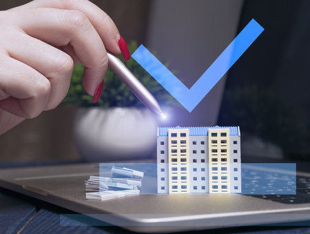 A hand using a stylus interacts with a virtual model of an apartment building on a laptop, symbolizing digital real estate investment.の写真素材