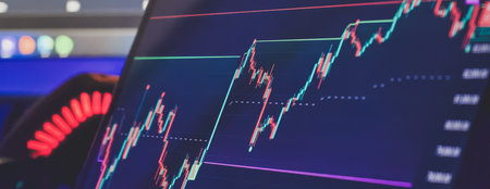 Close-up of a digital screen showing a candlestick chart with rising financial data and technical indicators in a dark setting.の写真素材