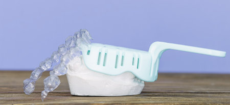 Clear orthodontic aligner placed on a plaster dental mold, with an impression tray in the background on a wooden surface.の写真素材