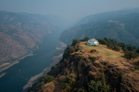 white house perched on a grassy cliff above a winding river canyon with dramatic rocky landscapes.の素材