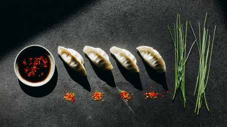 Close-up of golden crispy dumplings garnished with green onions, served with spicy soy dipping sauce, presented on a rustic slate plate.の素材
