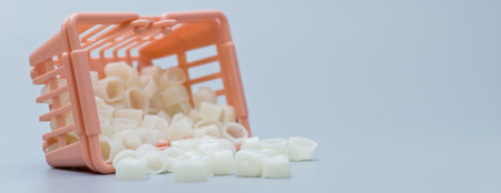 Plastic dental crowns spill out of an overturned miniature shopping basket, symbolizing dental care, treatment options, and healthcare costs.の写真素材