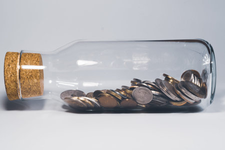 Glass jar with cork stopper and filled with international coins from various countries. transparent...