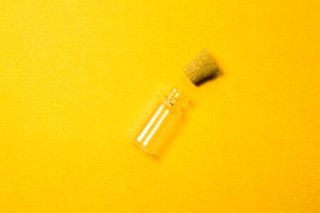 Empty little bottle with cork stopper isolated on yellow. glass vessel. transparent container. test tubeの写真素材