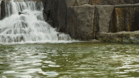 Small waterfall flows into a pond. rushing stream water background