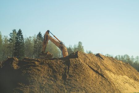 Excavator stands on the sand hill and digs the ground. part of construction earthmoving equipment. digging and filling the soil with an excavator bucketの写真素材