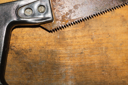 Old hand saw on a dirty wooden background. working area with hand tool. carpentry instrument. manual...