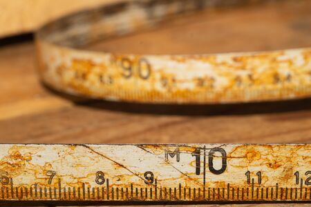 Old rusty ruler with black numbers on a working wooden table. vintage measuring tape close up. industrial background. carpentry workbenchの写真素材