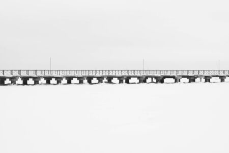 Bridge on the frozen lake. long footbridge dividing the horizon. conceptual minimalistic image. black and white background with copy spaceの写真素材