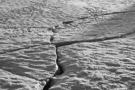 Cracked ice on the snow covered lake background. winter texture black and white