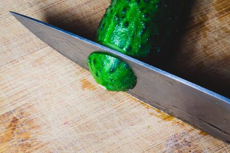 Cucumber and knife on a wooden cutting board. vegetable slicing process. cooking foodの写真素材
