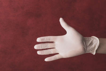 Palm of hand in medical glove on a red background. gesturing hand in white protective gloveの写真素材