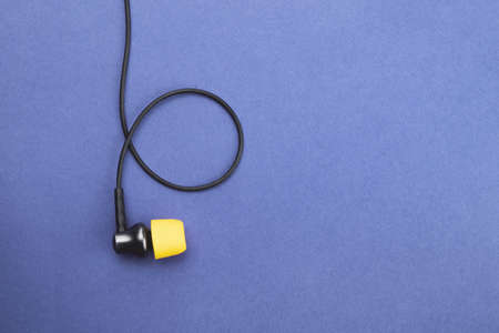 Earphone with yellow ear cushion on a blue background. in-ear headphones. audio equipment. copy spaceの写真素材