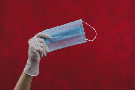 Blue medical mask in hand on a red background. preventive measures against respiratory illness and...
