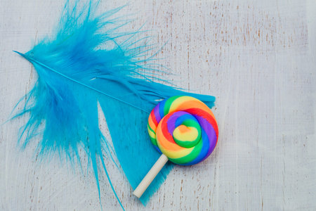 Lollipop lies on a feather. spiral candy on wooden background. festive decoration. copy space