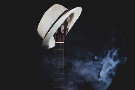 White hat hangs on the smoking guitar fretboard. acoustic musical instrument. strings on the guitar neck close upの写真素材
