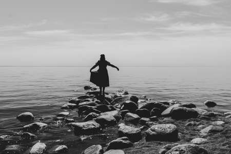 Silhouette of a woman standing on stones at the beach. beautiful summer landscape with horizon line. black and whiteの写真素材