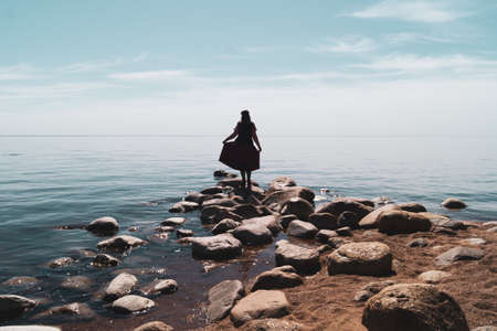 Silhouette of a woman standing on stones at the beach. beautiful summer landscape with horizon line. sea and skyの写真素材