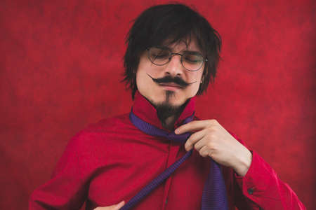 Young man takes off his tie. expressive male portrait on the red backgroundの写真素材