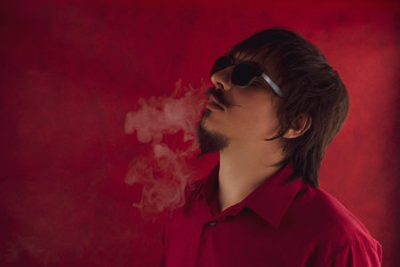 Young man exhales steam. male portrait on red background