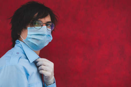 Young man in a medical mask with gloves and glasses on a red background. male portrait. virus protection measuresの写真素材