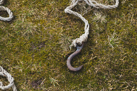 Rusty metal hook with rope lies on the green grass. marine equipmentの写真素材