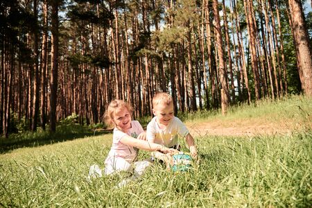 two small children in a pine forest laughing and playing with a ballの写真素材