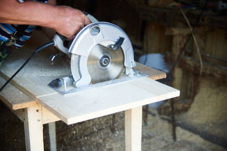a worker using a circular saw works with wood in a carpenters workshopの写真素材