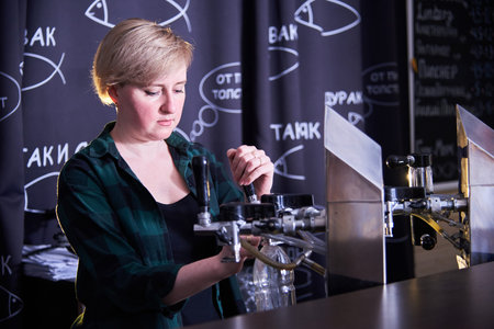 a young woman pours beer at the draught beer bar.Malt drink for international beer day