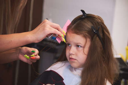 a little girl in a barbershop. Childrens haircut, hair drying, combing and styling. The child is happy and contented. Barber station wagon.の写真素材