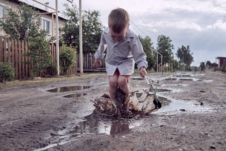 a boy jumps in a puddle on the street. Childhood in the country. The child is free and enjoys lifeの写真素材