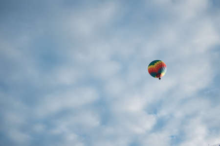 one multicolored balloon flies high in the sky covered with cloudsの写真素材