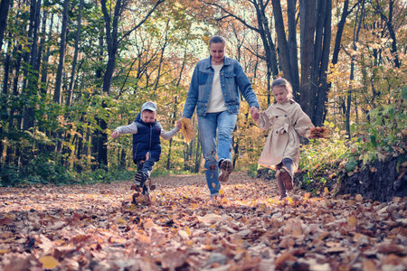 family walks in the autumn forest. Mother with two children running on fallen leaves.