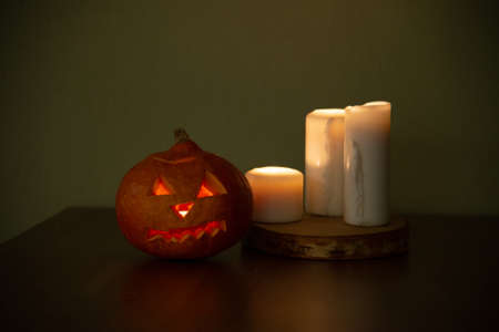 pumpkin with carved eyes for Halloween. A fire flickers inside the pumpkin, and large candles burn on the tableの写真素材