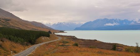 Stunning Panorama of Road Trip Scenery in New Zealand with the open road along a lake surrounded by big mountains. Photo taken in the Mount Cook Area.の写真素材