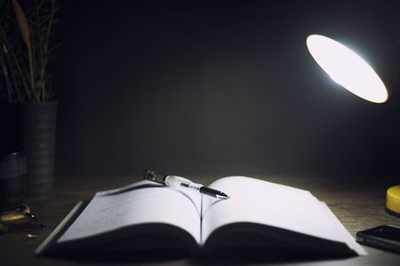 Reading table at night, With books, pen, lamps, Focus on the pen, Education concept.の写真素材
