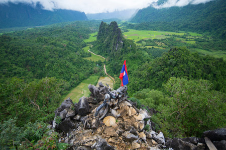 NAM XAY VIEWPOINT, VANG VIENG, LAOS - JULY 25, 2019: Ancient motorcycle parked and Lao flag on the Nam Xay Viewpoint, During the rainy season in Laos.のeditorial素材