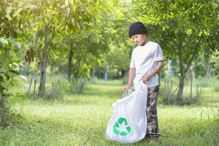 Boy keep the plastic bottle in the garbage bag, In green park area, Copy-spaceの写真素材