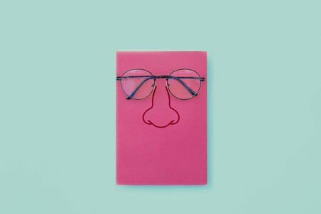 Glasses placed on pink book, Nose icon on book cover, On blue backgroundの写真素材