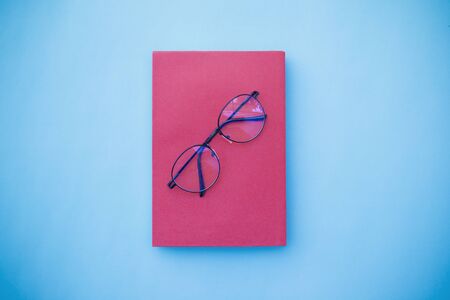 Glasses placed on pink book, Placed on blue background, Top viewの写真素材
